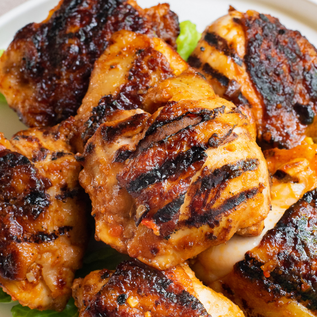Grilled harissa chicken thighs stacked on a white platter.