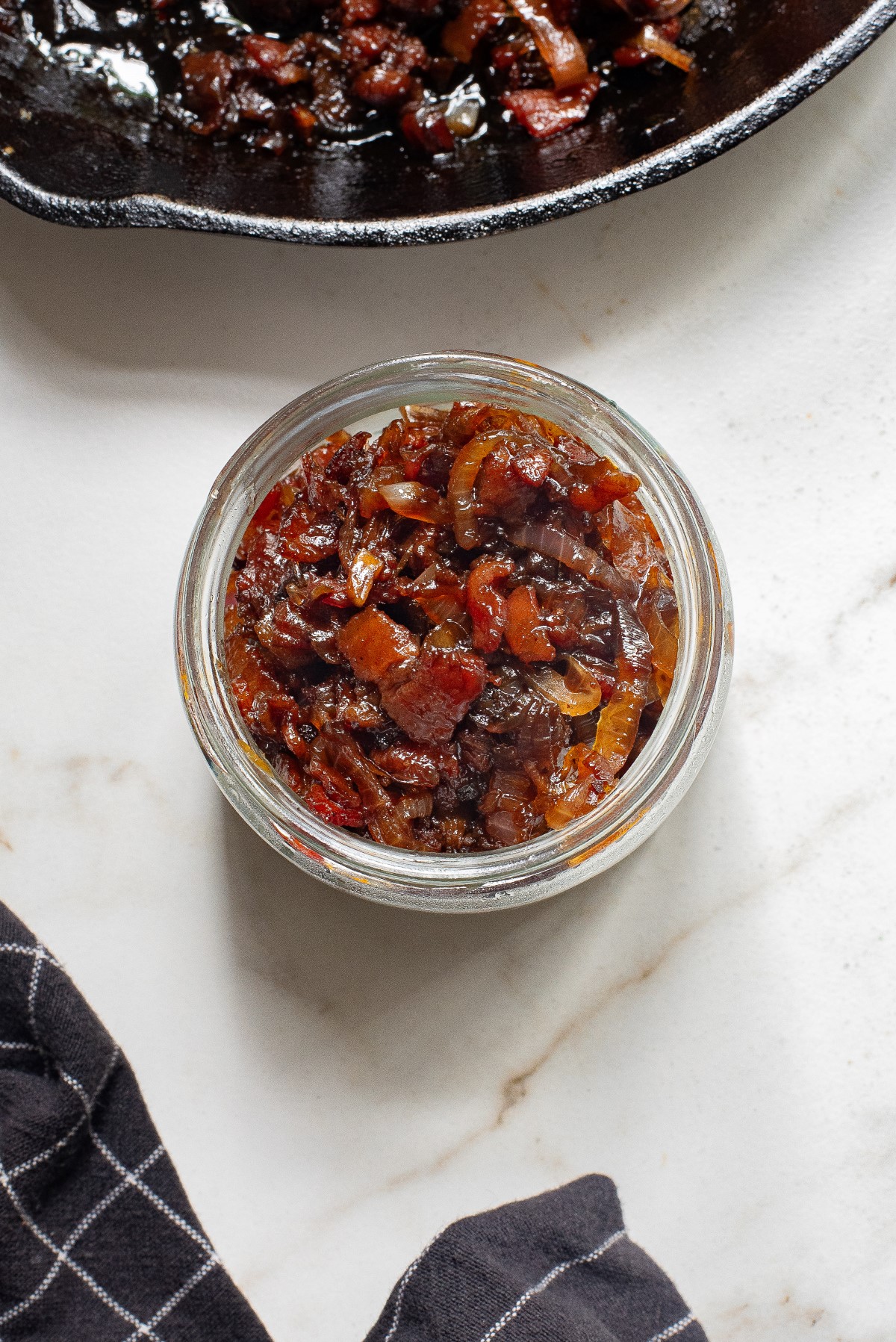 Onion bacon jam in a small jar beside a skillet of onion bacon jam.