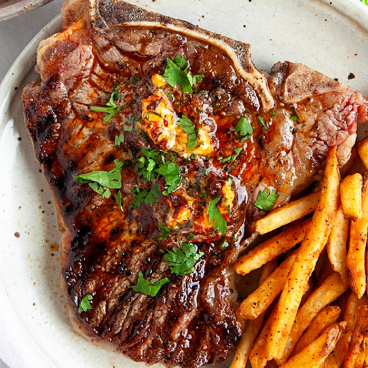 Grilled t-bone steak with chipotle cilantro butter on a plate with crispy fries.
