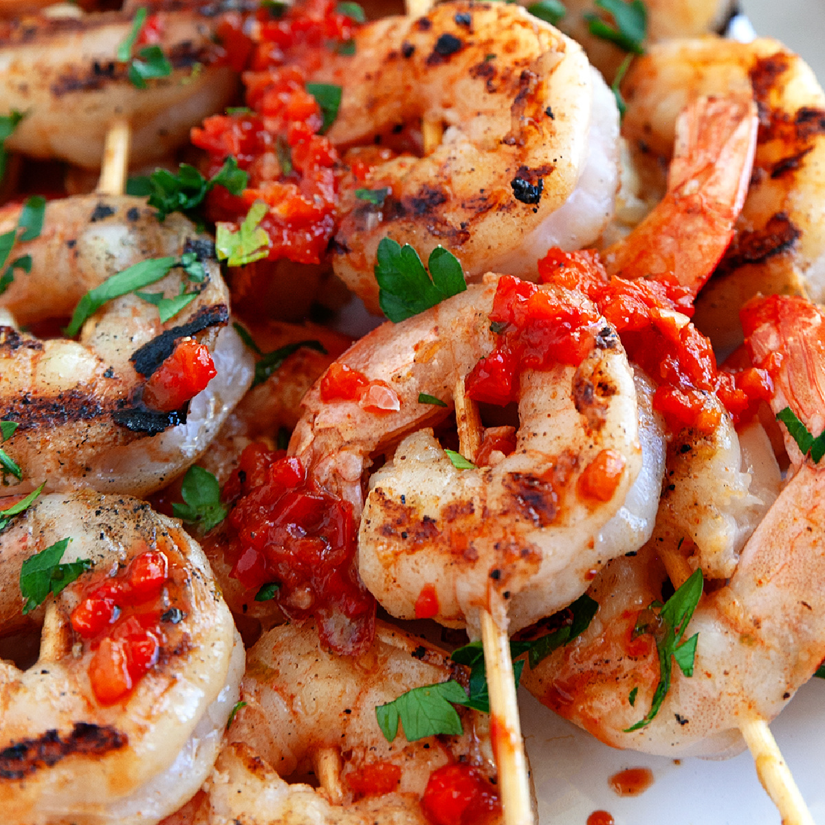 Grilled Shrimp Kebobs on a plate drizzled with red pepper sauce and garnished with chopped parsley.