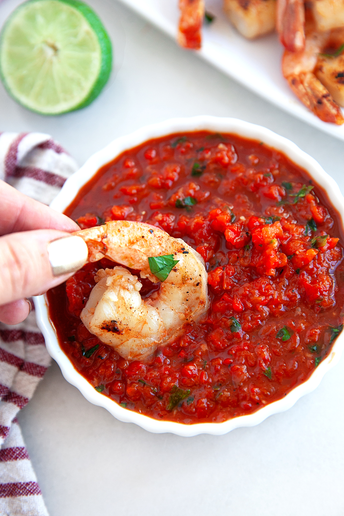 Grilled shrimp being dipped into a small bowl of red pepper sauce.