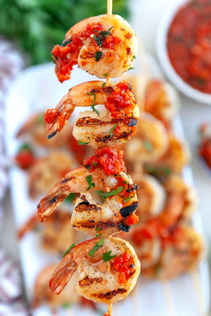 Grilled Shrimp kebobs on a wooden skewer held up with red pepper suace on the shrimp.