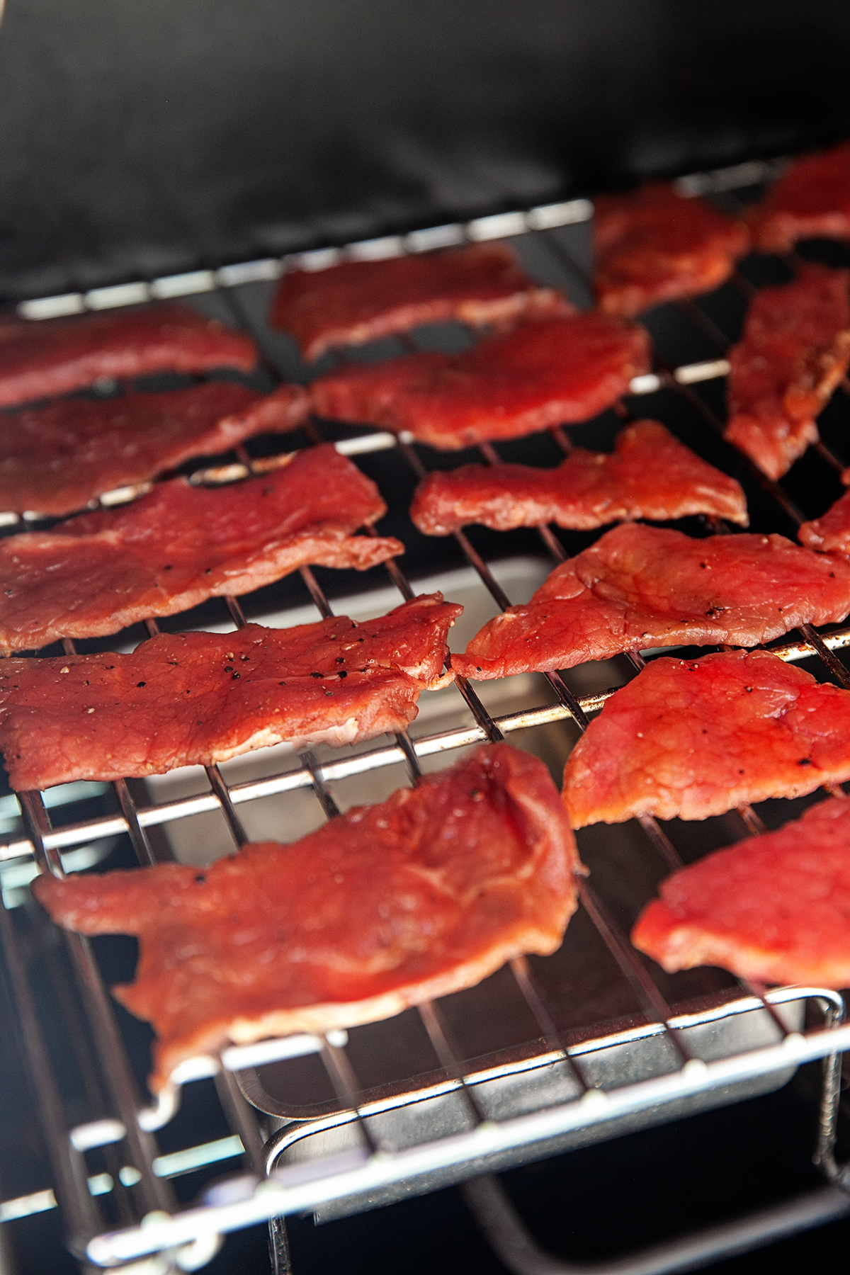 Coca-Cola marinated beef slices placed on a the racks of the smoker.