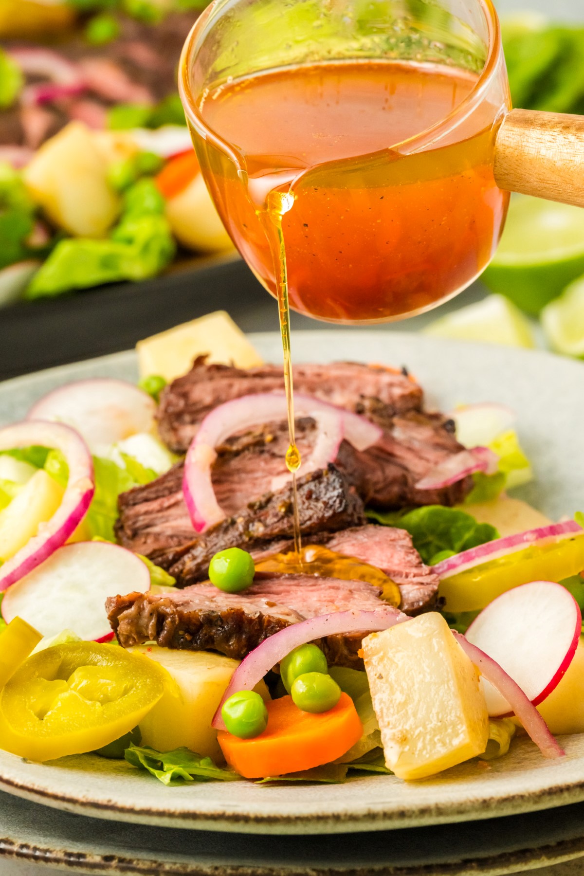 Drizzliing the dressing over the flank steak salad.