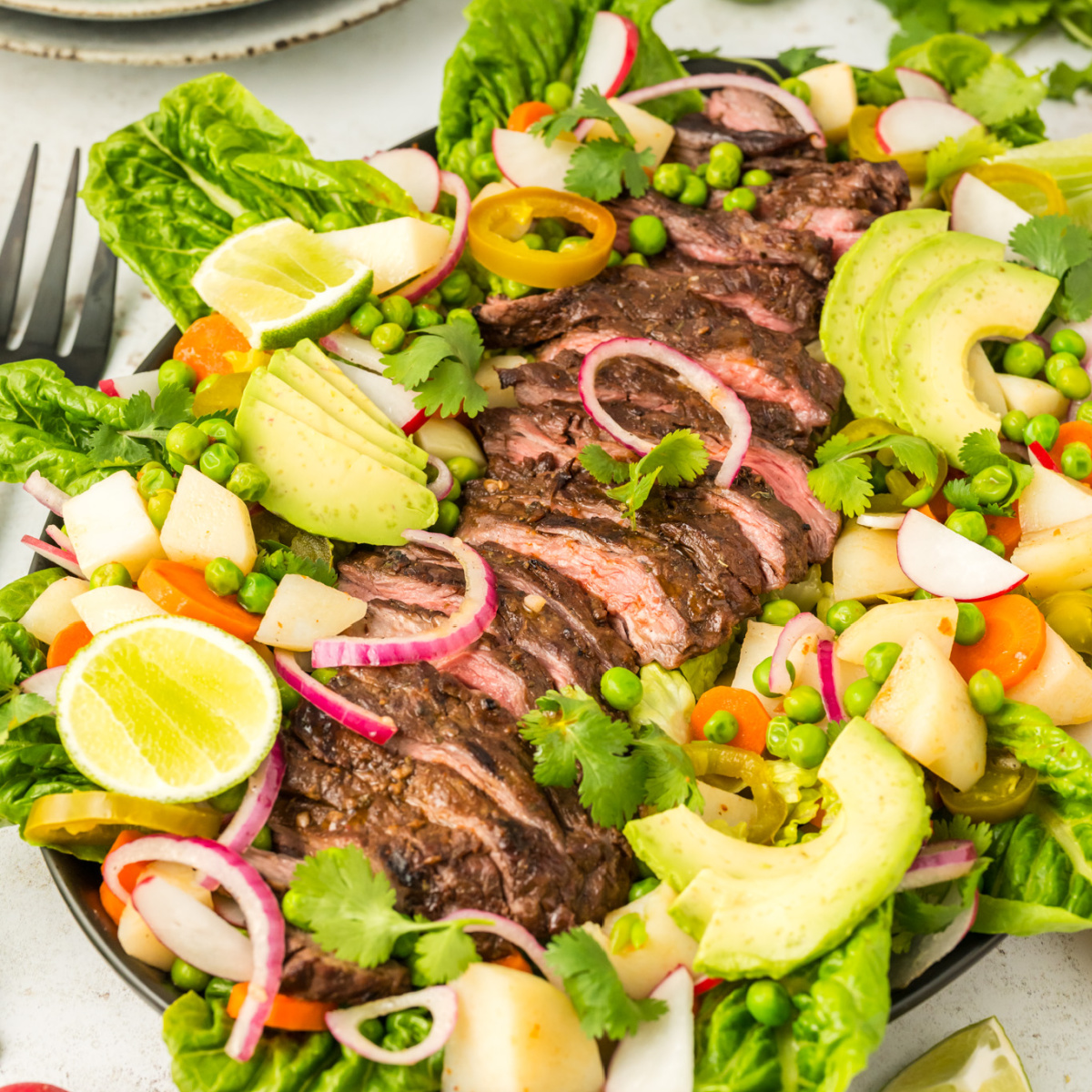 Sliced flank steak on a plate surrounded by vegetables.