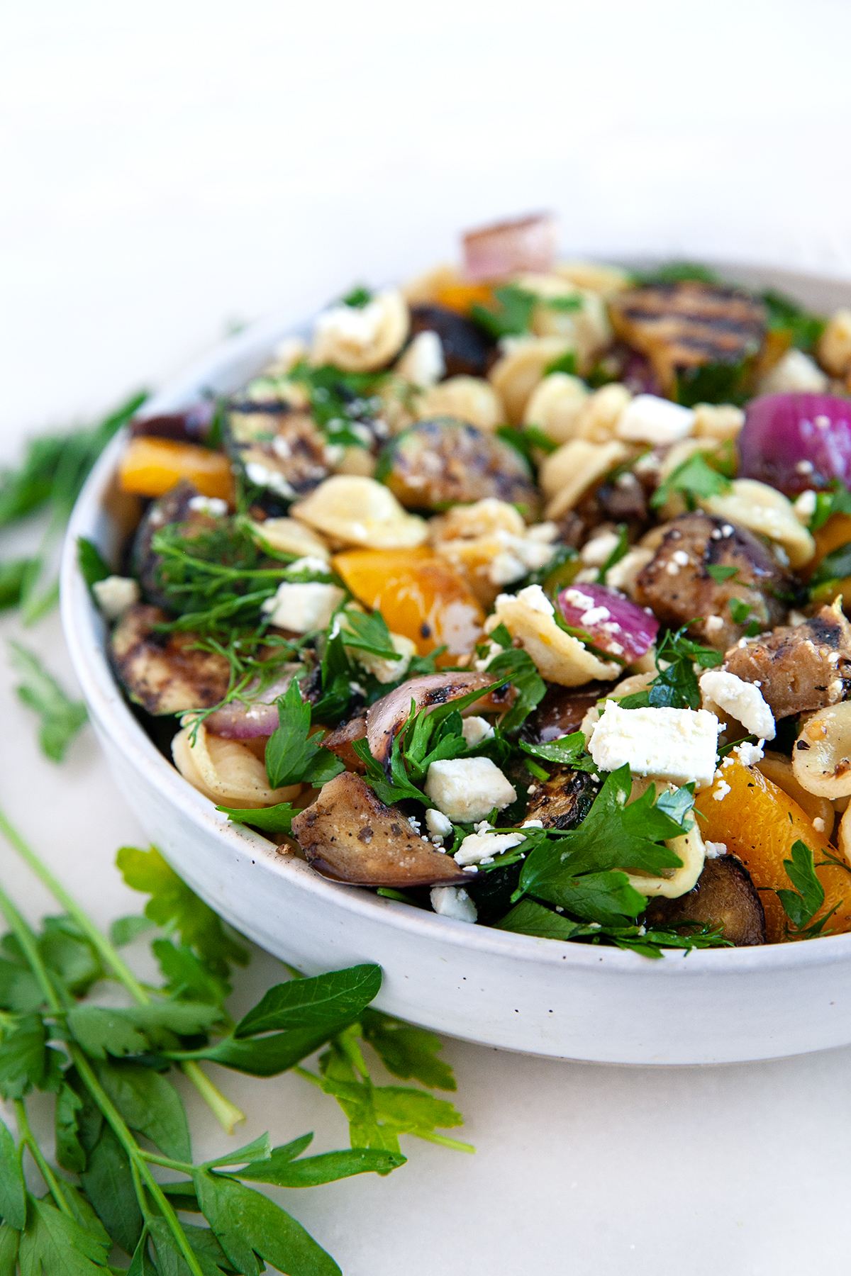 Grilled Vegetable salad with orecchiette pasta in a large serving bowl with sprinkled feta, chopped parsley and chopped dill on top.